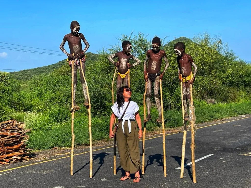 4 Karo tribe boys on stilts with traditional body paint posing with a tourist in Ethiopia